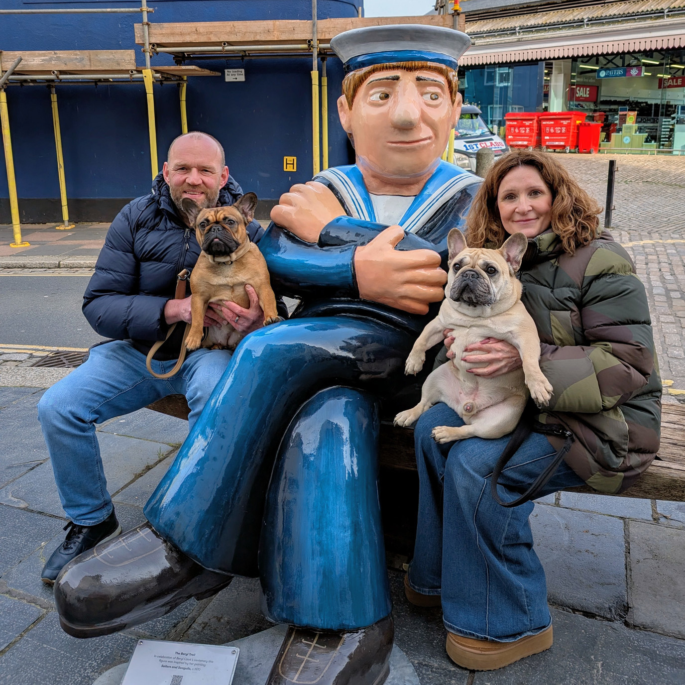 Two people and their dogs sat with the Beryl Cook sailor sculpture
